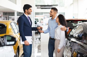 cheerful-sales-associate-giving-arabic-couple-key-from-car_116547-18495